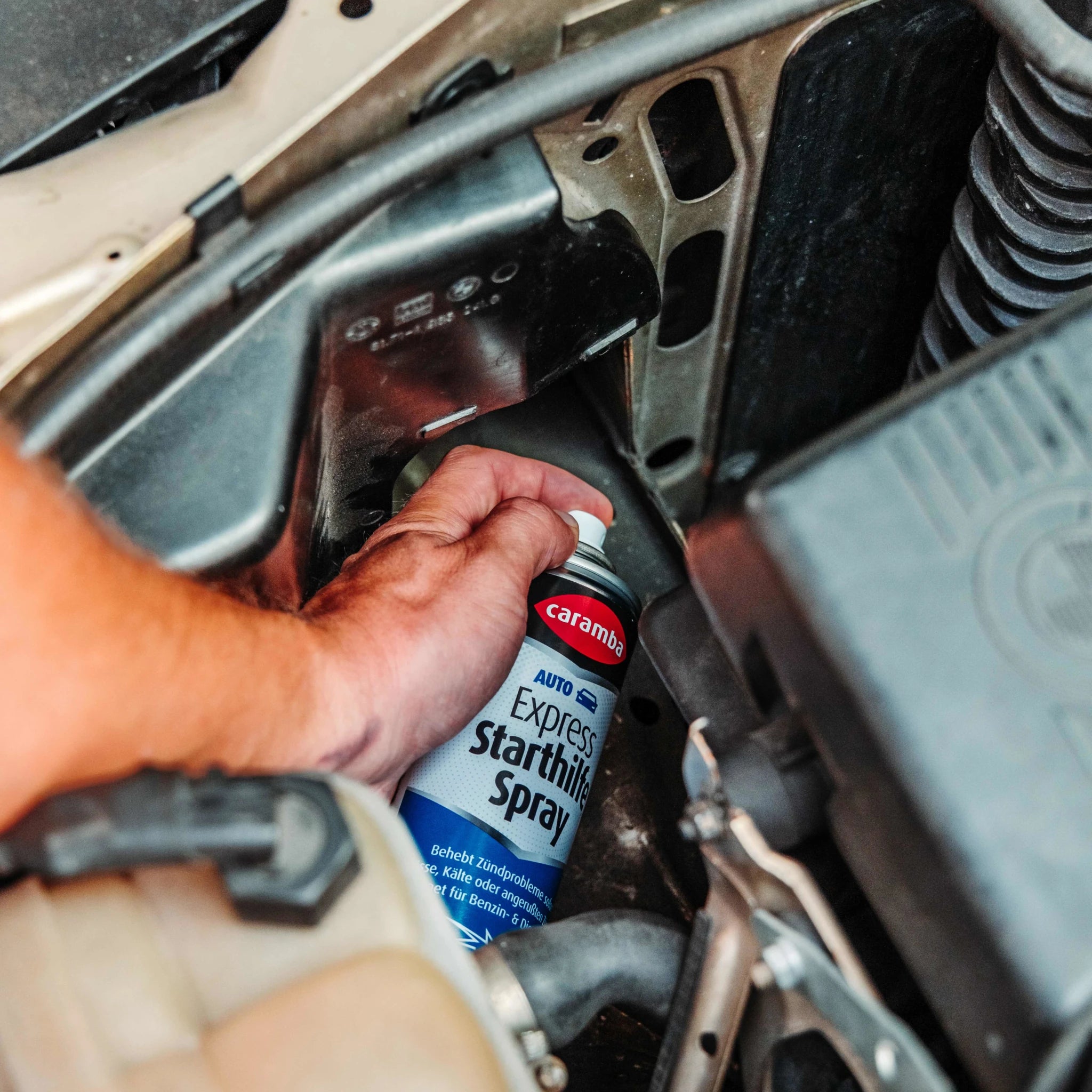 Bild der Anwendung des Caramba Starthilfesprays im Motorraum eines BMW